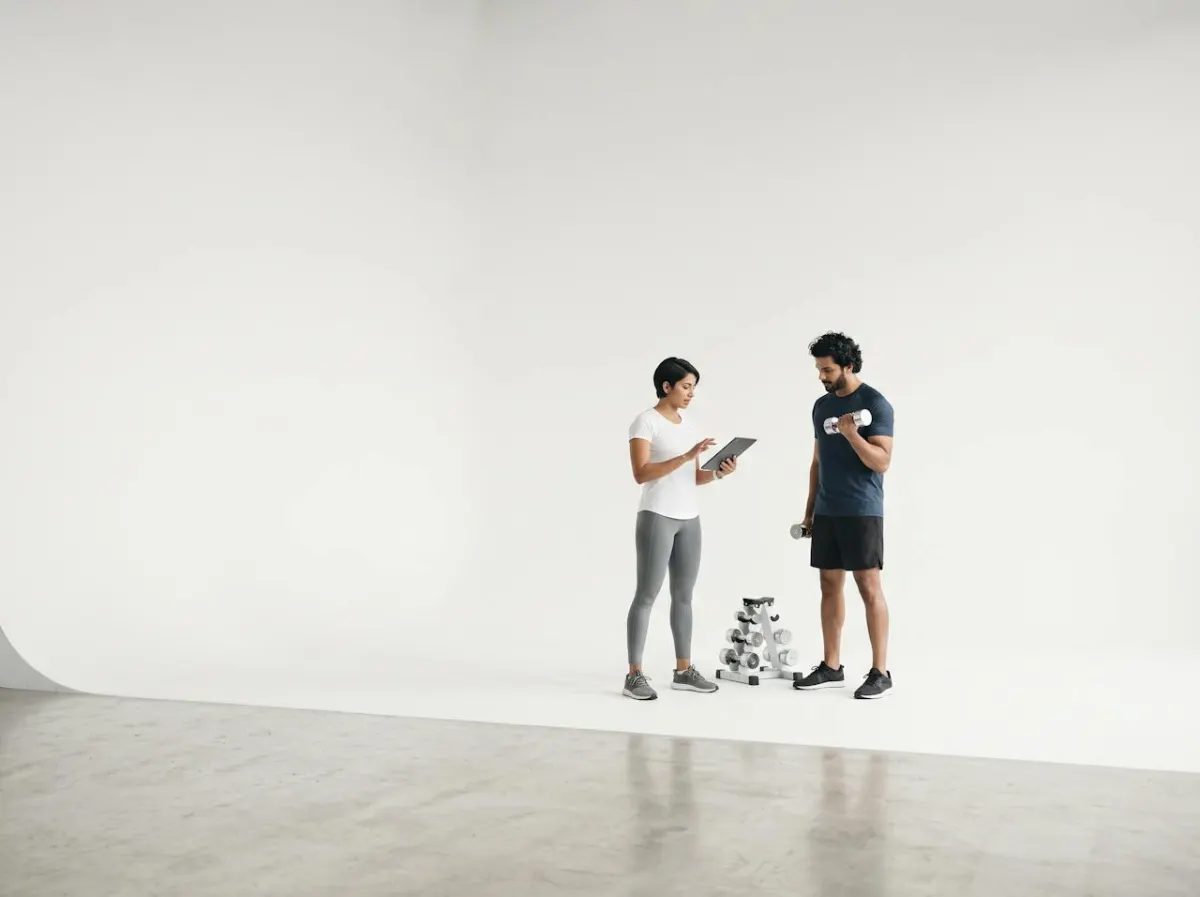A personal trainer holding a tablet while coaching a member with dumbbells