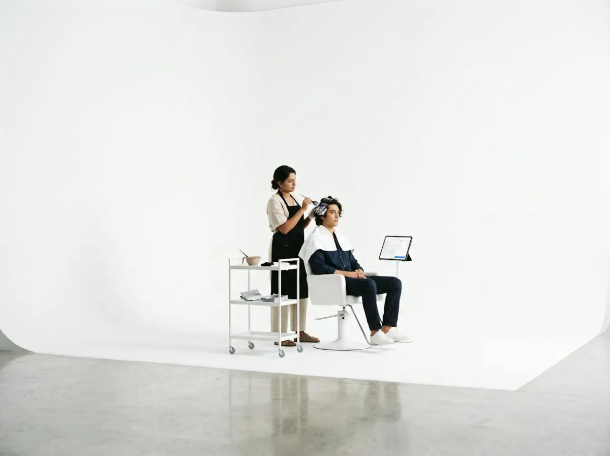 A stylist colouring a client's hair, with a tablet on the stand beside the chair
