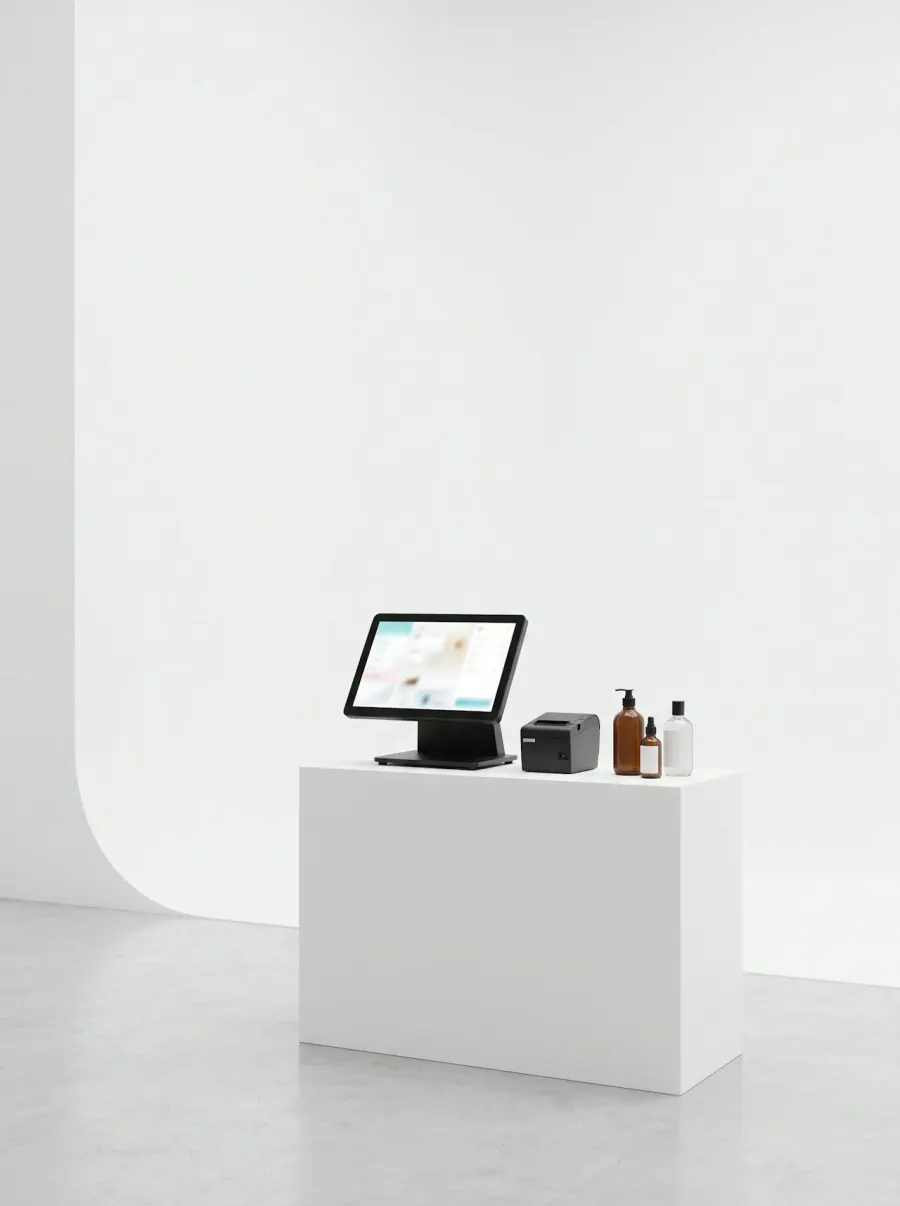 A single-screen POS terminal with a receipt printer and hair care bottles on a white counter